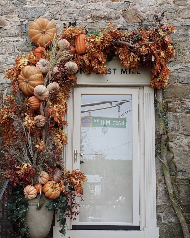 A Statement Entry as installed: a stone doorway framed by a sweep of dried oak leaves, wheat and pumpkins in orange, white and blush, rising from an urn to the lintel